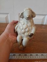 Front view of glazed pottery sheep figurine with ruler showing size