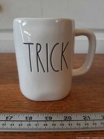 Front view showing "TRICK" text on white mug