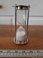 Full view of hourglass showing metal frame, glass bulbs and white sand with ruler indicating height