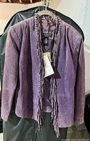 Front view of purple suede jacket on hanger showing fringe and tags