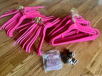 Group of hot pink velvet hangers with gold hooks and bag of clip adapters on wooden floor