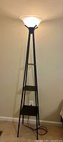 Full view of floor lamp illuminated showing frame, shelves, and shade