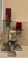 Three graduated silver-tone candle holders with pillar candles displayed together