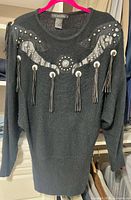 Front view of sweater showing appliqué, studs, fringe tassels