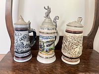 Front view of all three steins showing design details and lids