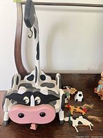Large wood cow pull toy with six small cow ornaments and figurines grouped beside