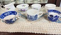 Seven pieces arranged: three violet cups, matching creamer, three blue transferware cups