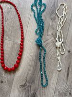 All three necklaces laid out: red graduated beads, teal faceted beads, white chip beads