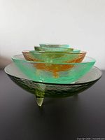 Six nested art glass bowls showing colours and tripod feet