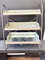 Front view showing three galvanized metal trays with mirror liners within metal frame