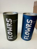 Two FLOWRS tins, green Botanical Gardens and blue Dreamy Delights, standing upright