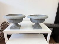 Full view of both gray pedestal urn planters on table