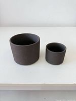 Large and small dark gray cylindrical concrete planters side by side