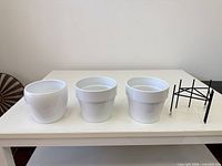 three white ceramic pots and one metal stand on table