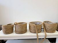Four woven seagrass baskets with plastic liners and straps displayed on table