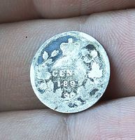 Reverse of worn 5 cent silver coin showing crown, maple leaves and partial date