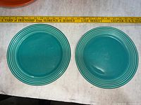 Front view of two teal Bauer dinner plates with tape measure showing size