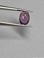 Oval pink-purple spinel held in tweezers showing table and crown facets