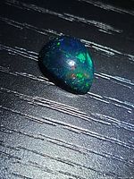 Top view of pear cabochon opal on dark surface showing play of colour