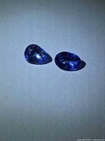 Two faceted tanzanite stones side by side on white surface