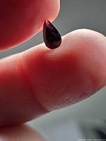 Pear-cut wine purple spinel held between fingers, shows overall size and colour saturation