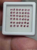Square gem case containing multiple small round pink-orange faceted stones