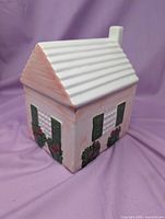 Front and side view of ceramic house cookie jar showing roof, walls, shutters and flowers