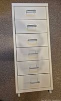 Front view of six-drawer white metal cabinet with handles and casters visible