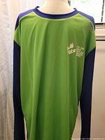 Front view of green and blue long-sleeve top with PEI 2023 Canada Games logo