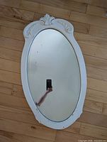 Front view showing white oval frame, carved crest, beveled mirror