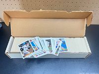 Open cardboard storage box filled with aligned baseball cards, small stack fanned in front