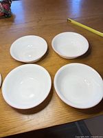 Four matching white bowls with pink rims on tabletop