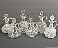 Front view of all six clear glass cruets standing side by side