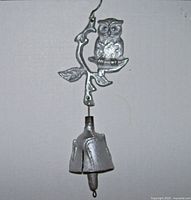 Full view of silver painted metal owl on branch with bell below