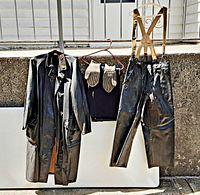 Front view of coat, pants with suspenders, winter liner, gloves hanging together