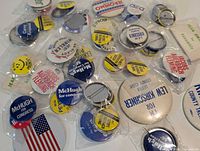 Overview of assorted political campaign buttons in plastic sleeves