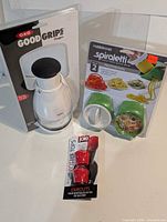Front view of all three sealed retail packages: OXO chopper, Farberware Spiraletti slicer set, Joie bottle tops