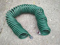 Entire coiled green hose arranged in horseshoe shape on concrete