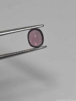 Faceted pink-purple spinel held in tweezers, showing cushion-oval shape
