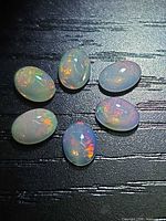 Six oval opal cabochons grouped on black background displaying fire