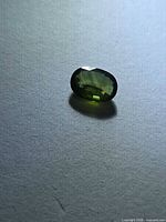 Oblique view of loose oval faceted green sapphire showing color and shape