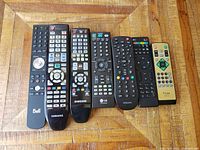 All seven remotes laid out on wooden surface