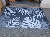 Full view of grey and white plastic leaf-pattern rug