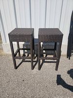Two matching dark brown woven rattan bar stools front view