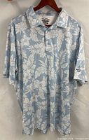 Front view of light blue and white hibiscus print polo shirt on hanger