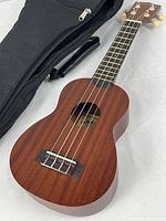 Full view of Makala soprano ukulele beside black gig bag