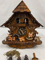 Front view of wooden chalet cuckoo clock showing animated figures, dial and carvings