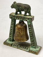 Full view of brass souvenir bell showing bear, frame, bell and inscriptions