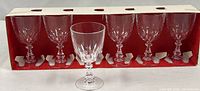Six crystal wine glasses arranged in original red box with one glass displayed in front