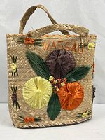 Full view of woven straw tote with embroidered flowers and Nassau lettering